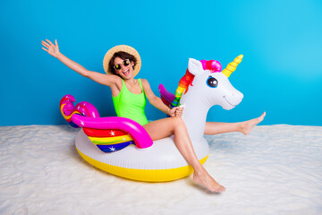 Wall Mural - Excited Young Woman Posing With Colorful Unicorn Float Toy on Sandy Beach With Blue Background