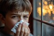 © Oleksandr - Boy with stuffy nose wipes his face with a napkin while looking out the window at sunset
