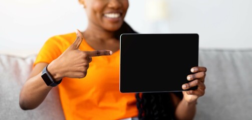 Poster - Internet purchases concept. Positive black woman pointing at tablet screen with mockup for shopping app or website design at home, selective focus. Happy African American lady buying gifts on web