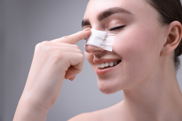 Wall Mural - Woman with medical bandage on her nose after plastic surgery operation against grey background