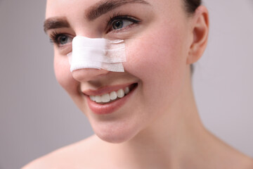 Wall Mural - Woman with medical bandage on her nose after plastic surgery operation against grey background