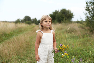 Cute little girl with flowers at meadow. Child enjoying beautiful nature