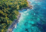 Aerial view of turquoise water and lush green coastline with rocky shore and forest
