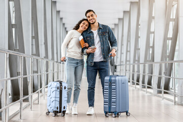 Wall Mural - Portrait Of Cheerful Young Middle Eastern Couple Standing At Airport With Luggage And Smartphone, Millennial Arab Man And Woman Air Travelling Together, Ready For Vacation Trip, Copy Space