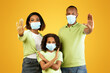 © Prostock-studio - Social distancing and Covid-19 pandemic. African american parents and their daughter in medical masks showing STOP gesture on yellow studio background