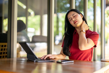 A woman in a red shirt is sitting at a table with a laptop and a cell phone