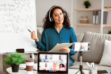 Aufkleber - Online Training. Young lady tutor in headset teaching online by video conference using laptop and smartphone. Teacher explaining information to diverse participants in the virtual conference