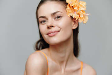 Poster - Young woman with orange flower, showcasing a bright smile against a soft gray background. Ideal for seasonal beauty or fashion concepts.