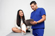 © Arlette - Woman with broken leg in a cast in the office of a dark-skinned Latino doctor who treats her for pain and recovery