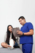 © Arlette - Woman with broken leg in a cast in the office of a dark-skinned Latino doctor who treats her for pain and recovery