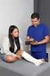 © Arlette - Woman with broken leg in a cast in the office of a dark-skinned Latino doctor who treats her for pain and recovery