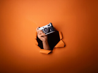 Leinwandbilder - A hand emerges from a torn orange background, holding a vintage camera.  The scene is minimalist and evokes a sense of mystery and creativity.