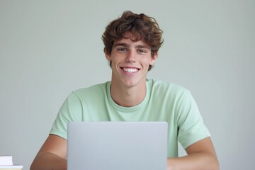 Wall Mural - A young man is sitting at a desk with a laptop in front of him. He is smiling and he is enjoying himself