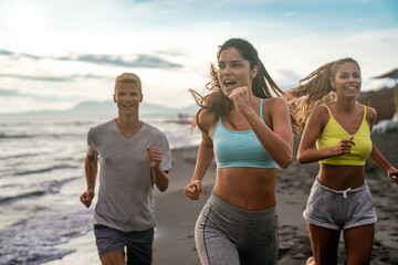 Wall Mural - Group running on beach jogging having fun training. Exercising runners training outdoors