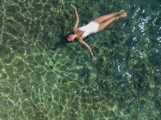 girl in white swimsuit lies on water in sea drone view