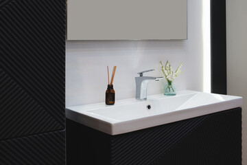 Poster - A bathroom sink with a vase of flowers and a bottle of essential oil on the counter. The sink is white and the counter is black