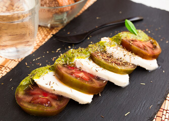 Wall Mural - Caprese salad with mozzarella, black tomatoes and pesto on black stone plate