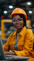 Aufkleber - Young woman wearing safety glasses and a hardhat, focused on working with a laptop in a busy factory environment