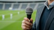 © fotogurmespb - Elegant A sports reporter holding a microphone on the sidelines of a soccer game with the field and players in motion behind them