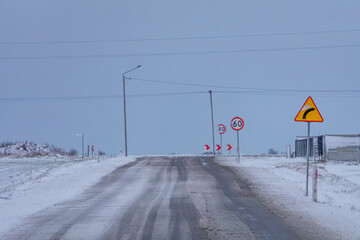 Wall Mural - sudden attack of winter. snow, frost, ice. bad weather conditions on the roads. difficult and capricious weather conditions. snowdrifts in the field. road sign about left turn and speed limits