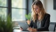 © kotlyarn - A young woman with long, wavy hair is intently working on a tablet in a stylish office space filled with natural light. Her professional attire and serene expression reflect dedication and creativity