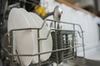 © Ксения Мнасина - Close-up of open dishwasher department with clean plates and cutlery against kitchen background: white cabinets and wooden countertop out of focus. The concept of washing dishes, cleanliness
