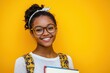 © Diana - Smiling student holds books against a vibrant yellow backdrop in a cheerful study atmosphere