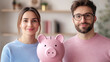 © NeeNA - Young couple smiling with piggy bank, representing financial planning and savings