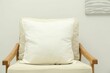 © New Africa - Blank soft pillow on cozy armchair near light grey wall indoors