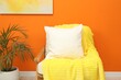 © New Africa - Blank soft pillow on cozy armchair near orange wall indoors