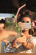 © blackday - Woman Capturing a Toast with Drinks at an Outdoor Cafe