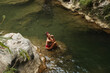 © blackday - Woman in a red swimsuit sits on a rock in the middle of a calm jungle stream