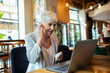 © Davor - Senior businesswoman enjoying coffee while working on laptop at cafe