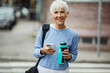 © Davor - Senior woman checking phone while walking with gym gear and water bottle