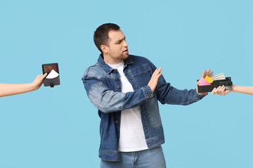 Wall Mural - Young man refusing wallet with credit cards on blue background