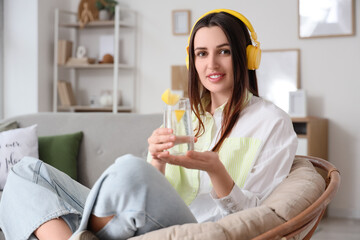 Poster - Beautiful young woman with lemon infused water and headphones sitting in armchair at home