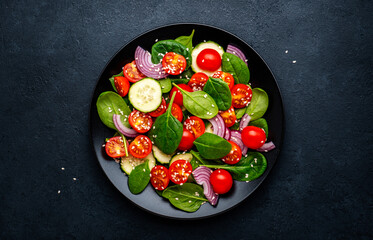 Wall Mural - Healthy vegetable salad with spinach, tomatoes, cucumber and red onion. Black table, top view