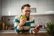 © Miljan Živković - happy adult man eat apple for nutrition and use mobile phone