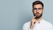 © khonkangrua - Young man with beard and glasses pondering an idea against a light blue background in a casual white shirt