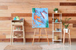© Pixel-Shot - Painting on easel with shelving units and art supplies near brown wooden wall