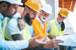 © Dragana Gordic - Construction Workers Collaborate on Site Plan Wearing Protective Gear Outdoors