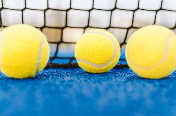 Wall Mural - three balls in front of the net of a blue paddle tennis court padel background concept