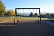 © syafiamin - Serene Playground Scene Featuring Empty Swings in Bright Sunlight Surrounded by Greenery and Mountainous Backdrop Under Clear Blue Sky