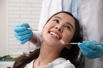 Wall Mural - Close-up shot of beautiful Asian female face, white teeth, and cheerful face in dentist's hand, dental treatment with tooth whitening and cleaning in doctor hospital clinic, oral hygiene healthcare.