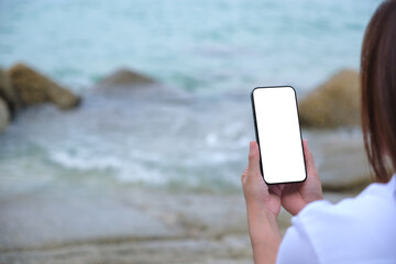 Wall Mural - mockup image of a woman holding mobile phone with blank desktop screen on the beach
