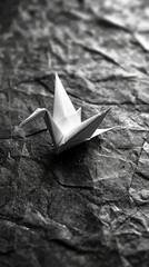 Poster - A delicate paper crane resides upon a crinkled, dark surface, showcasing intricate folds and a timeless elegance. The artwork captures the essence of simplicity and craftsmanship
