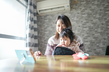 A Japanese mother in her 20s and a 6-month-old baby girl are in the room. She is putting on makeup while looking at her smartphone.