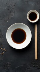 Poster - A serene dining setup features a white plate filled with rich dark soy sauce, accompanied by a small cup and delicate chopsticks, all arranged against a textured dark background