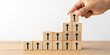 © Theerawat - Hand placing wooden block with upward arrow on a growing stack of similar blocks symbolizing progress and growth