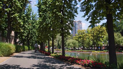Aufkleber - Biking along a scenic path with trees and flowers near a tranquil waterway in a vibrant urban park
